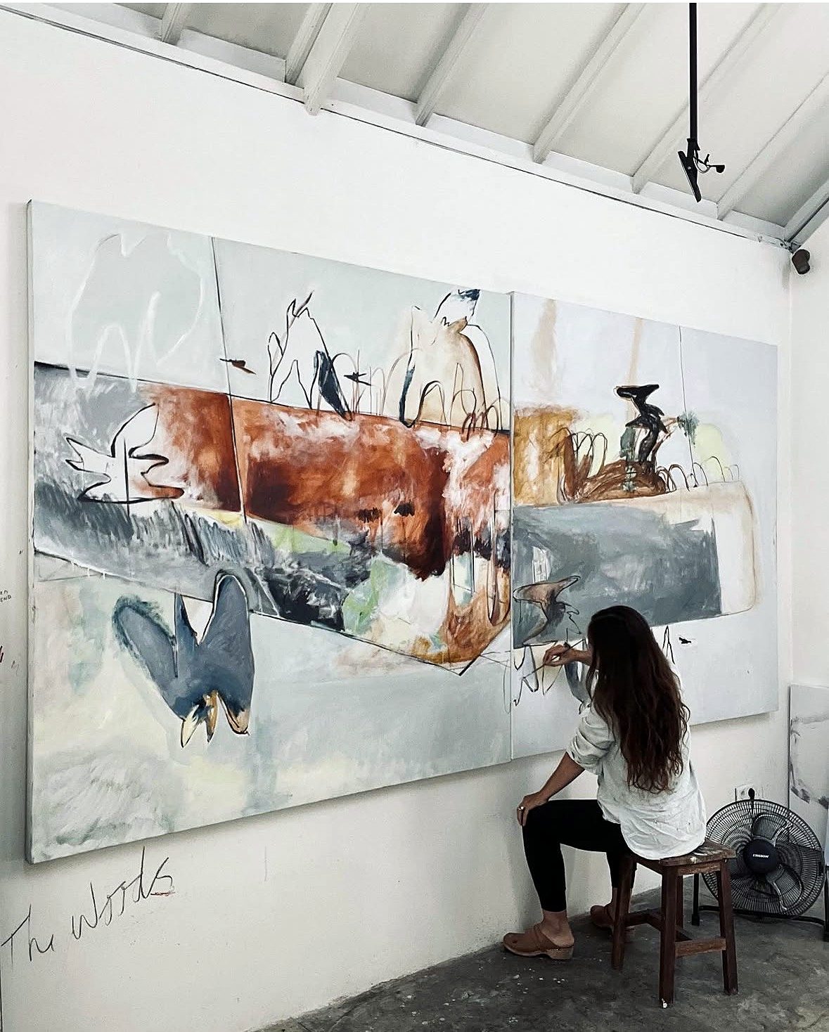 Lydia Janssen seated on a stool, working on The Housebirds on the studio wall